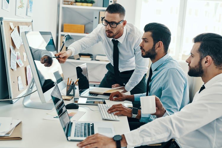 Men stand around screen and discuss