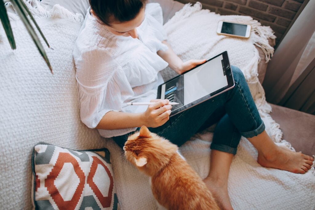 Woman sits on sofa with tablet and ginger cat