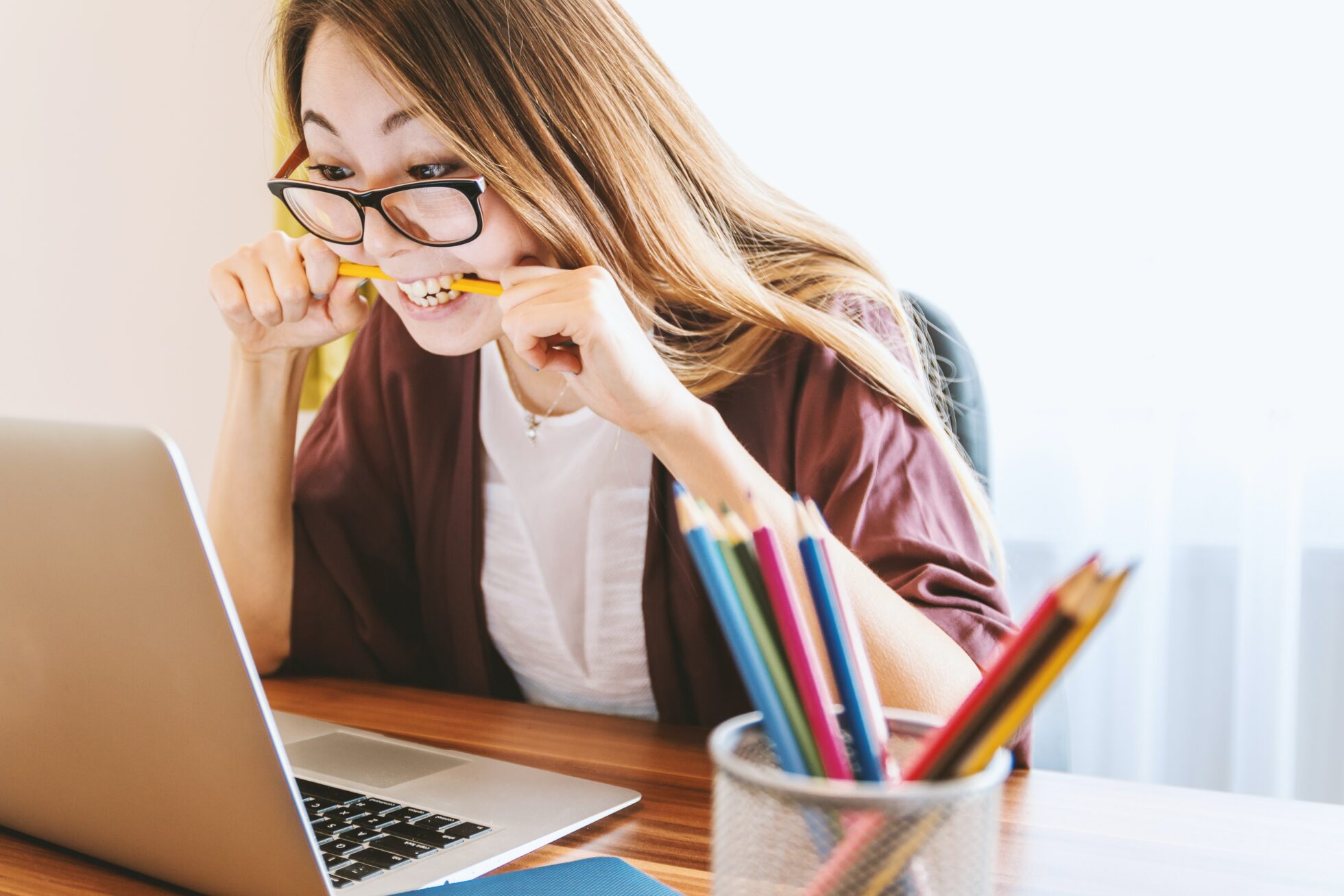 Woman chews on pen in frustration while looking at laptop screen