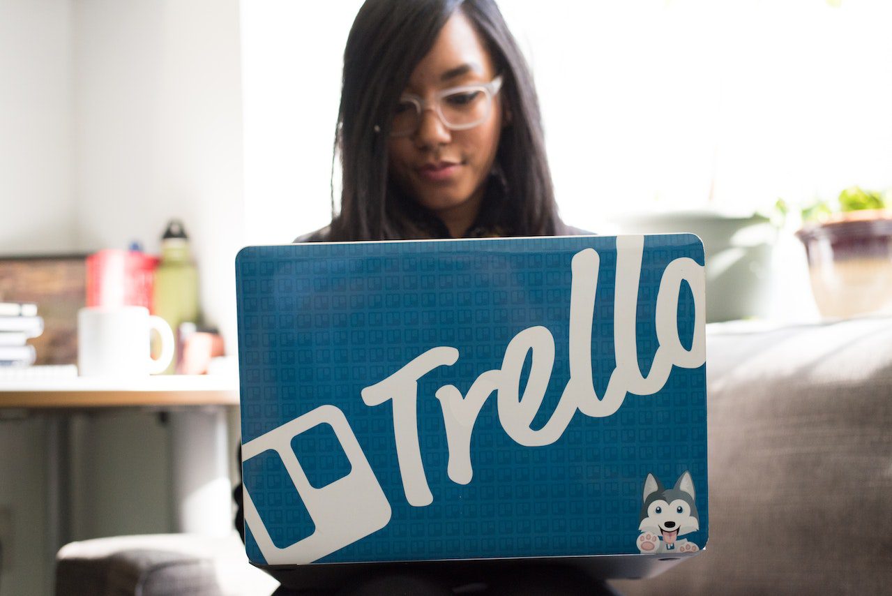 trelloのブランドロゴを背負ったノートパソコンに向かう女性像