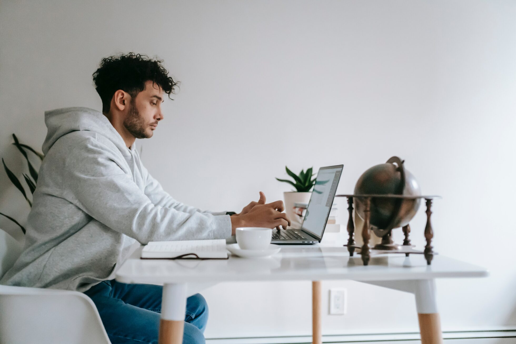 Sideview of someone in a white hoodie typing on a laptop while working remotelya