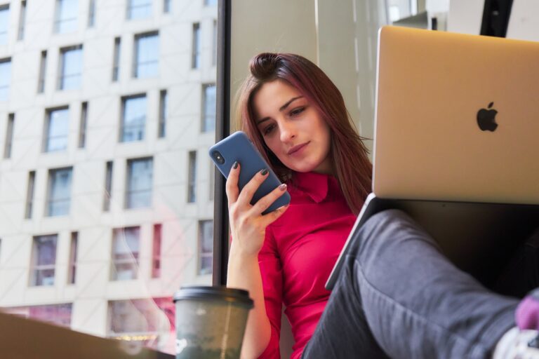 노트북에 앉아 휴대폰을 보며 remote 작업 도구를 사용하는 여성