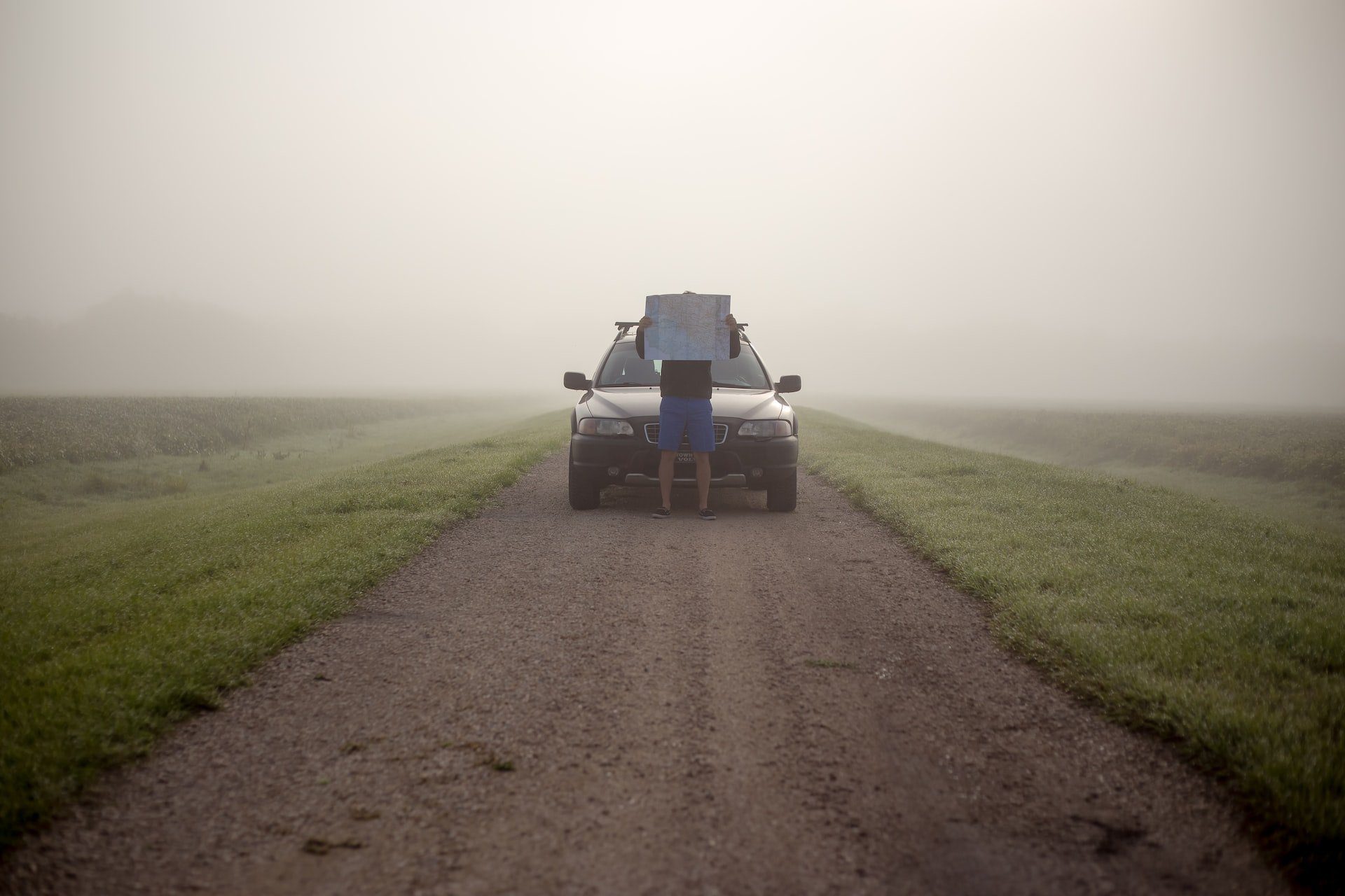 imagem de uma pessoa em pé na frente de um carro em uma estrada com neblina e um mapa na mão