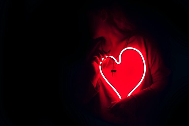 person holding a neon heart sign in the dark