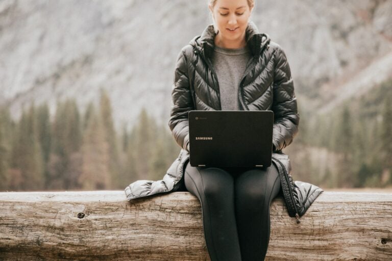 woman sat on a log working on a laptop remotely as a virtual assistant