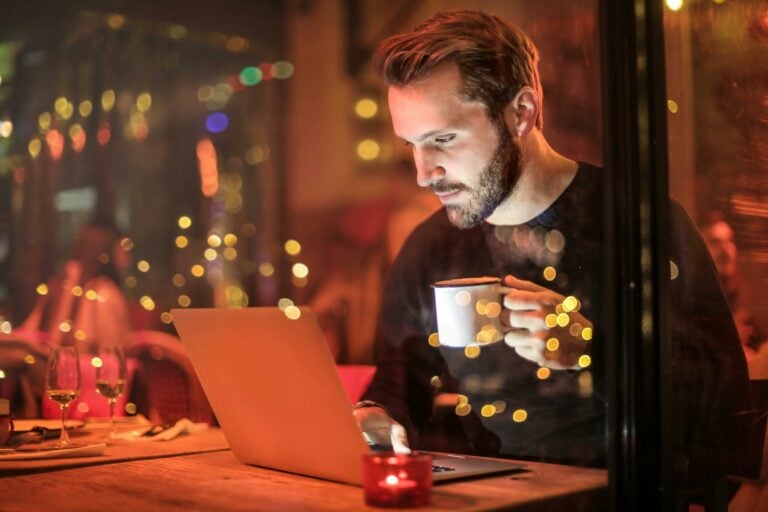 image of a man holind a coffee and using a laptop to illustrate the concept is microsoft teams free?