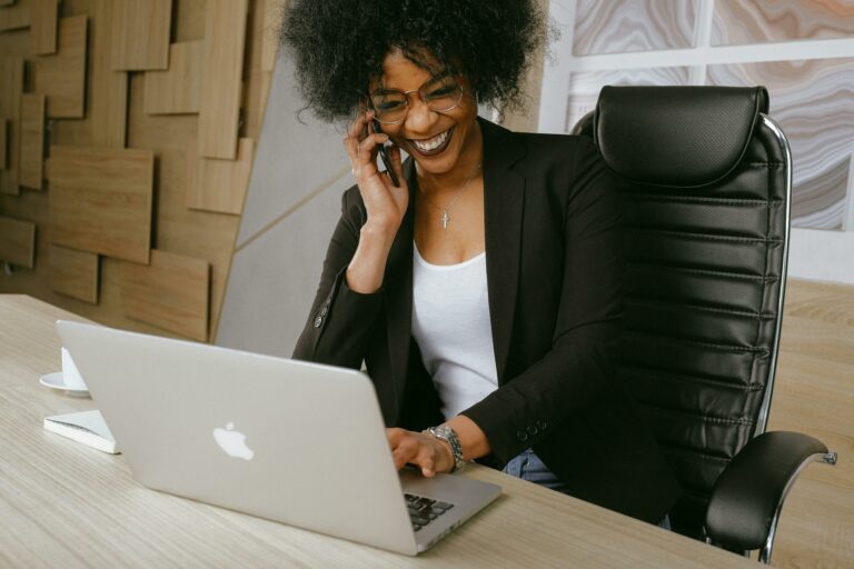 señora en un ordenador portátil sonriendo mientras sostiene una llamada para representar la mejora de los guiones de llamadas en frío