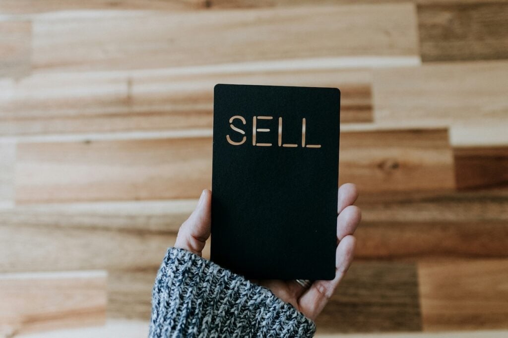 Image of a woman&#039;s hand with a grey jumper holding a black card that says SELL for SPIN SELLING