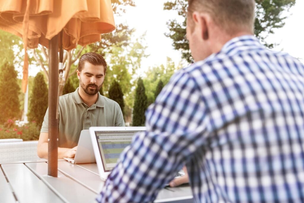 Image of two men on laptops at a table to illustrate conversational intelligence for sales